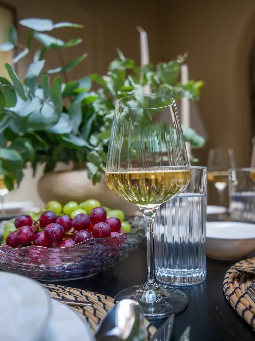 A dining table laid with white wine, grapes and eucalyptus